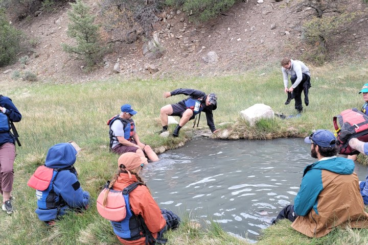 People in life vests gather around a small pond in a grassy area.