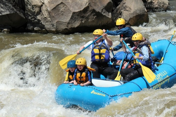 Group rafting in a blue boat navigating whitewater rapids.