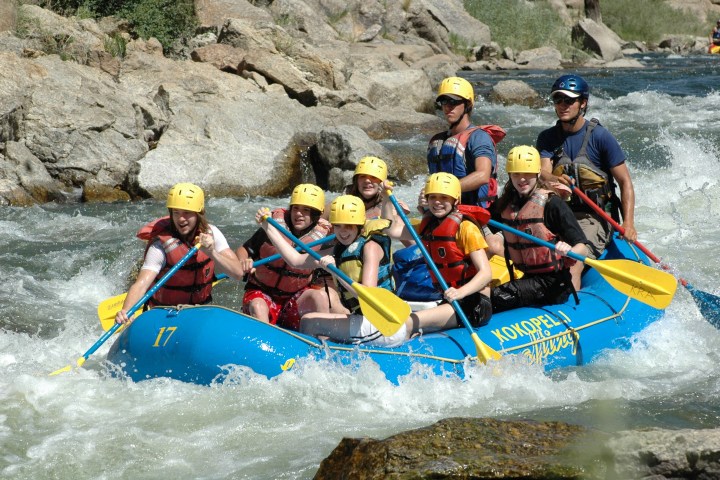 Group in helmets and life vests white-water rafting on a rocky river.