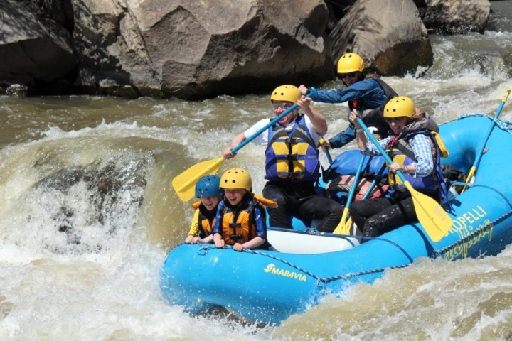 Group of people whitewater rafting in a blue inflatable raft on a rocky river.