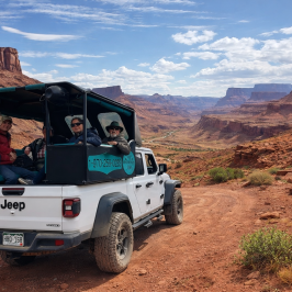 Open-top Jeep with passengers on a rocky road in a canyon landscape.