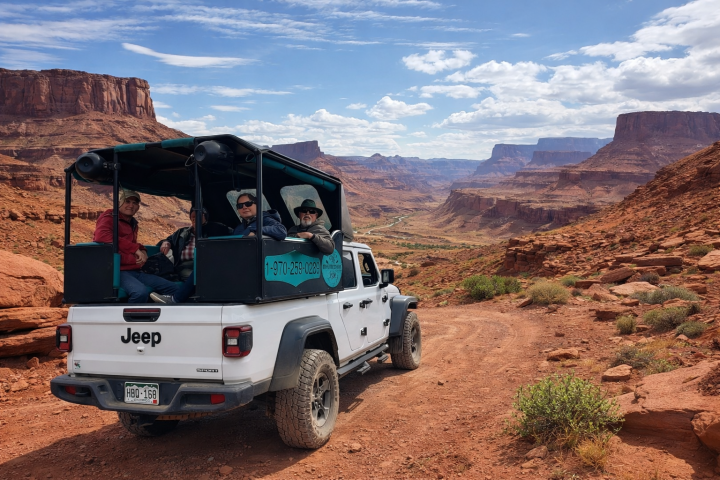 Open-top Jeep with passengers on a rocky road in a canyon landscape.