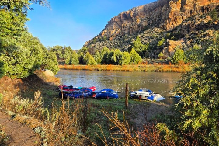 Inflatable rafts on a riverbank with rocky cliffs and trees in the background.