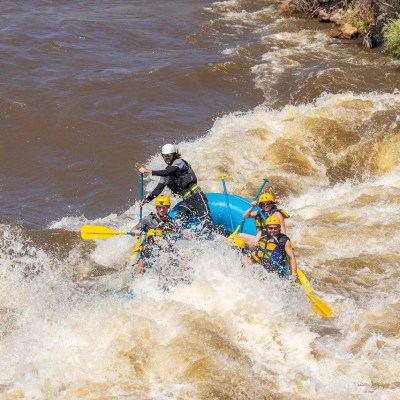 Group whitewater rafting on turbulent river in a blue raft with helmets and paddles.